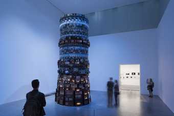 Man looking at a tall tower of old electronics in a blue lit room in the Tate Modern