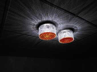 Two textured glass lamps with orange-brown liquid in them attached to a tiled ceiling