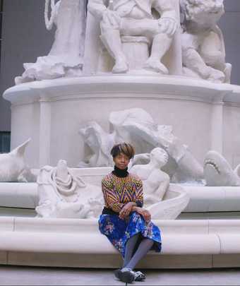 artist kara walker sitting on rim of large white fountain
