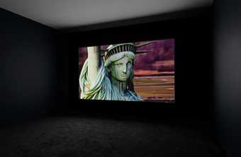 installation of a film screened in a blacked out room. the projection shows a close up of the face of the statue of liberty in new york.