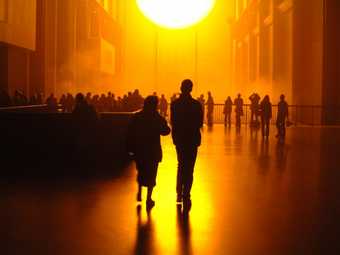Two people walk towards a large artificial sun in Tate Modern's Turbine Hall