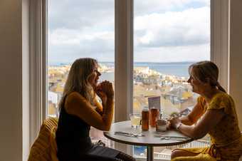 two women sit by a window with some drinks